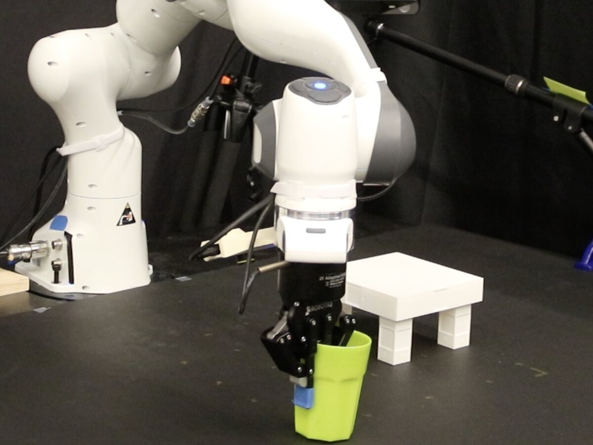 A Franka Panda arm grasping a green cup, about to place it upright on a small white table