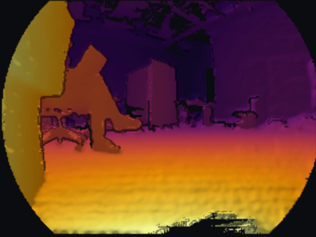 Depth image from the Odin, colored from yellow for near to purple for far, in its round fisheye frame: a wall close by on the left, a person sitting in a chair, and boxes and furniture across the room