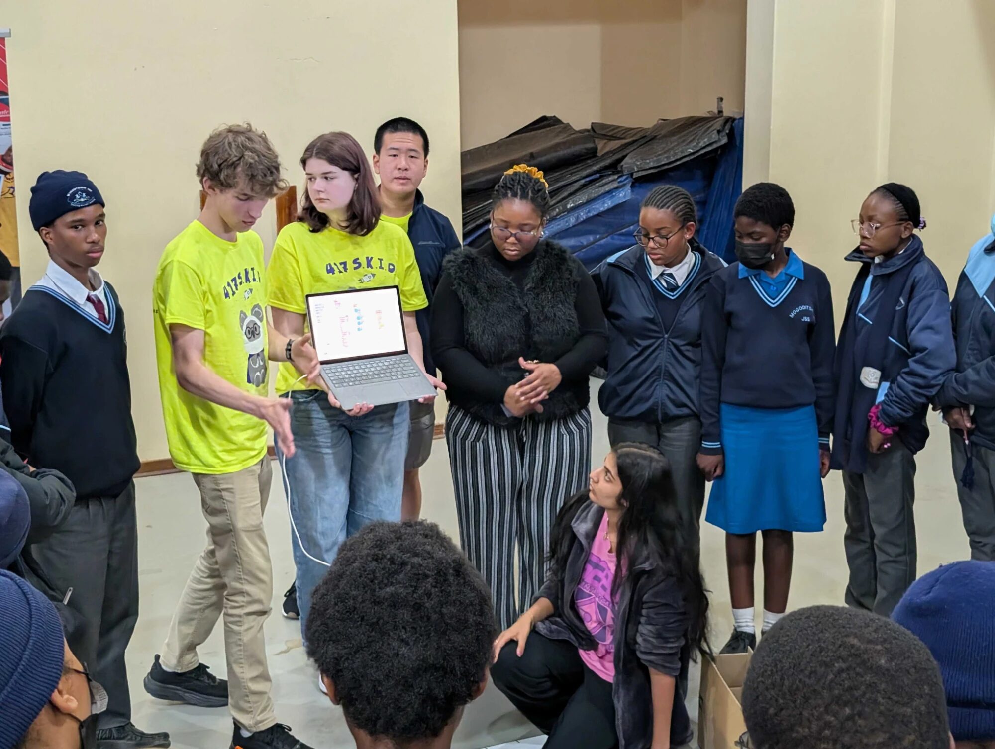 Eric holding up a laptop of block code for a group of students in school uniforms, with teammates beside him